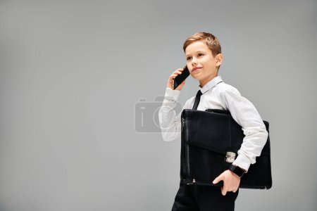 A stylish boy holds a briefcase and talks on a cell phone.