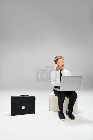 Foto de Niño en traje elegante se sienta en el taburete, absorto en el ordenador portátil. - Imagen libre de derechos