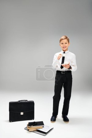 A preadolescent boy in elegant attire standing next to a suitcase, embodying a business concept.