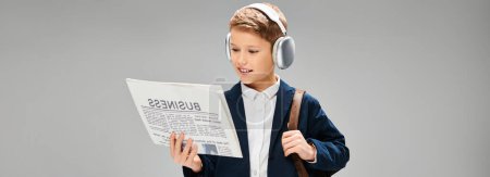 Young boy in elegant attire, wearing headphones, engrossed in reading newspaper.