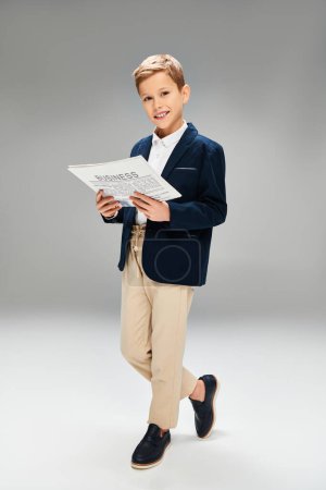 A dapper boy in a blue blazer and khaki pants engrossed in reading.