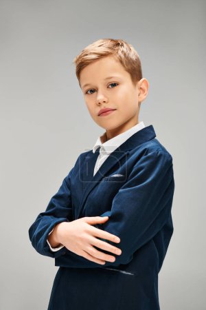 Preadolescent boy in elegant blue suit standing with arms crossed.