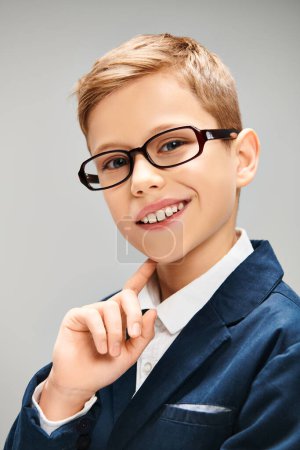 A young boy in glasses strikes a pose in his elegant attire against a gray backdrop.