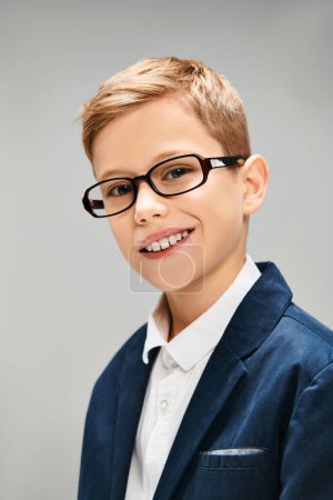A young boy in a suit and glasses on a gray backdrop.