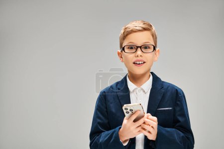 Foto de Elegante niño preadolescente en gafas con teléfono celular sobre fondo gris. - Imagen libre de derechos