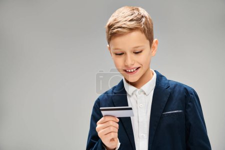 Kleiner Junge in eleganter Kleidung untersucht Kreditkarte.