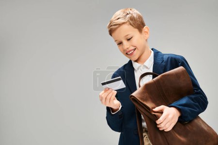Preadolescent boy in elegant attire holding briefcase and credit card.