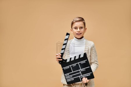 Foto de Joven niño se esconde juguetonamente detrás de una tabla de aplausos mientras está vestido como un director de cine. - Imagen libre de derechos