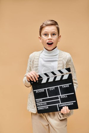 Photo for A young boy disguised as a film director holds a clap board in front of his face. - Royalty Free Image