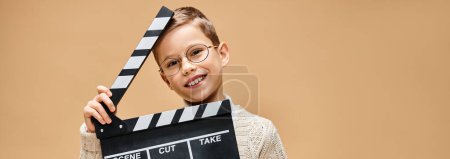 Téléchargez les photos : Un garçon préadolescent imite un réalisateur avec une planche à claquettes. - en image libre de droit
