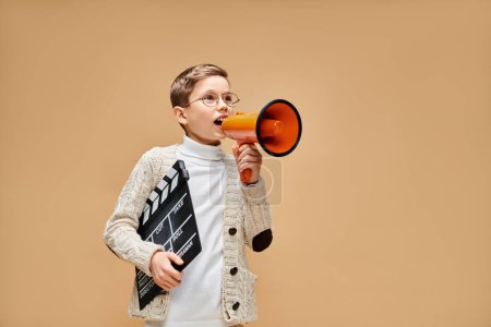 Téléchargez les photos : Un jeune garçon habillé en réalisateur tenant un mégaphone rouge et orange. - en image libre de droit