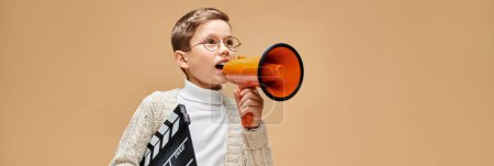 A preadolescent boy dressed as a film director, holding a red and orange megaphone.
