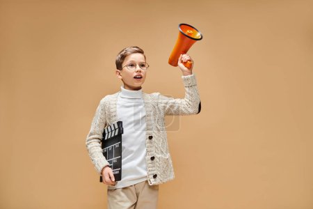 Téléchargez les photos : Un jeune garçon, habillé en réalisateur, tient un mégaphone et un battant. - en image libre de droit