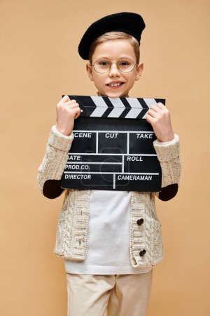 A preadolescent boy holding a clapper board in front of his face.
