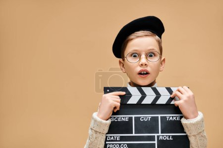 A cute preadolescent boy, dressed as a film director, holds a movie clapper in front of his face.