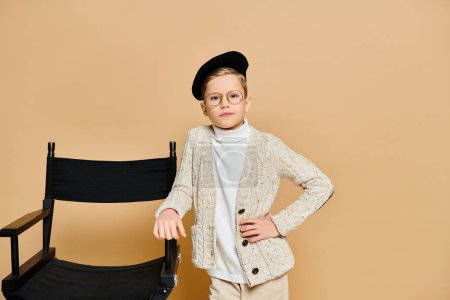 A cute preadolescent boy dressed as a film director standing next to a chair.