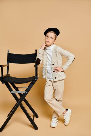 Preadolescent boy in film director attire stands beside a chair.