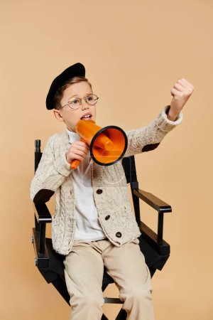 A preadolescent boy, dressed as a film director, sits in a chair holding an orange megaphone.