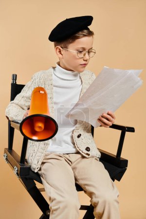 Als Filmregisseur verkleideter vorpubertärer Junge, der auf einem Stuhl sitzt und ein Blatt Papier hält.