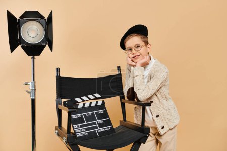 Preadolescent boy dressed as a film director stands next to a camera.