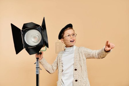Un lindo niño preadolescente vestido como director de cine, sosteniendo una cámara y una luz.