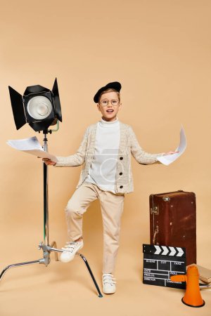 Preadolescent boy dressed as a film director on beige backdrop.