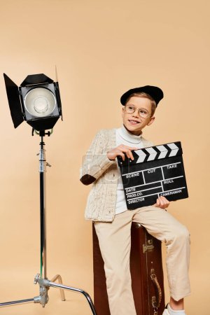 Young boy in director costume poses with movie clapper in front of camera.
