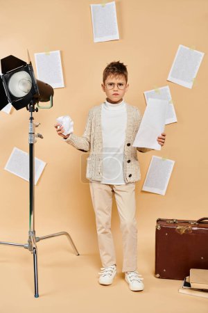 Preadolescent boy dressed as a film director on a beige backdrop.