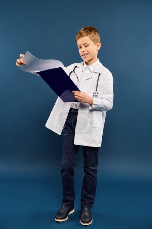 Young boy in lab coat holding clipboard on blue backdrop.