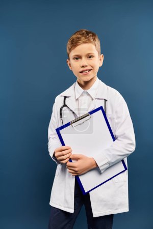 A preadolescent boy in a doctors coat holding a clipboard on a blue backdrop.