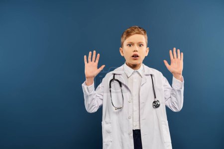 A preadolescent boy in a white lab coat, hands raised, on a blue backdrop.