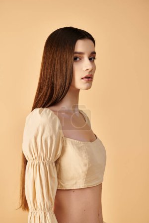 A young woman with long brunette hair, embodying a summer mood, poses gracefully in a white top in a studio setting.