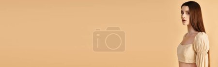 Foto de Una joven con el pelo largo y morena posa en un traje de verano contra una pared bronceada, exudando un humor radiante de verano. - Imagen libre de derechos