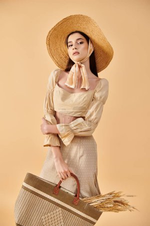 Stilvolle junge Frau mit langen brünetten Haaren, Hut und Kleid, in dem sie einen Korb hält, verkörpert ein sommerliches Ambiente in einem Studio-Ambiente.
