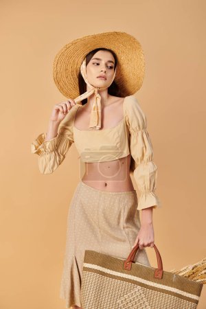 Mujer joven con el pelo largo y morena emana vibraciones de verano, sosteniendo una bolsa de paja en un elegante sombrero de paja.