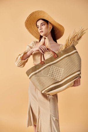 Téléchargez les photos : Jeune femme aux longs cheveux bruns frappant une pose estivale, rayonnant d'élégance dans un chapeau de paille tout en tenant un sac. - en image libre de droit
