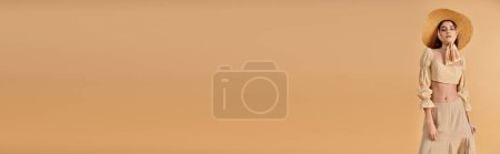 Téléchargez les photos : Une jeune femme aux longs cheveux bruns se tient sur la plage portant un chapeau de paille, rayonnant d'ambiance estivale et profitant de l'atmosphère sereine. - en image libre de droit
