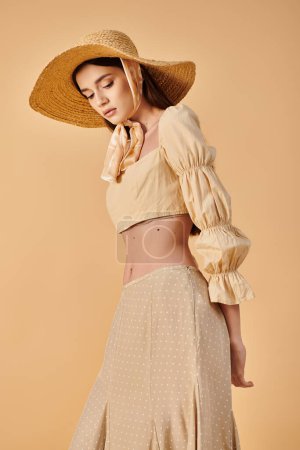 A fashionable young woman with long brunette hair striking a pose in a stylish hat and skirt, exuding a summery vibe in a studio setting.