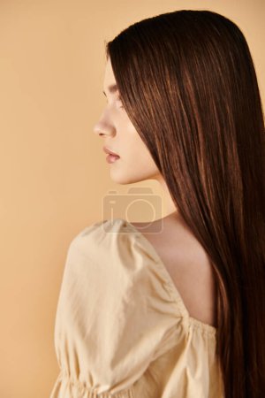 Une jeune femme aux longs cheveux bruns pose en toute confiance dans une tenue d'été dynamique contre un mur uni.