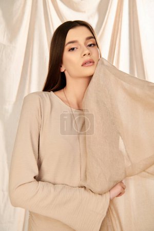 Photo for A young woman with long brunette hair strikes a pose in a beige top, exuding a serene summer mood in a studio setting. - Royalty Free Image