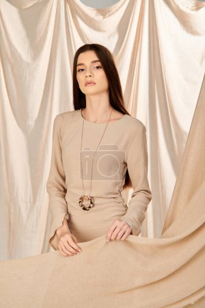 A young woman with long brunette hair in a beige dress posing elegantly for a summer-themed photo shoot in a studio setting.
