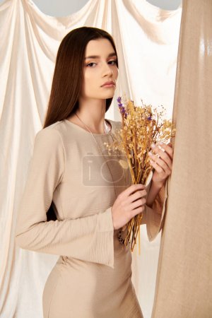 Eine junge brünette Frau im sommerlichen Outfit hält einen Blumenstrauß vor einen Vorhang, der eine fröhliche und lebendige Energie ausstrahlt.