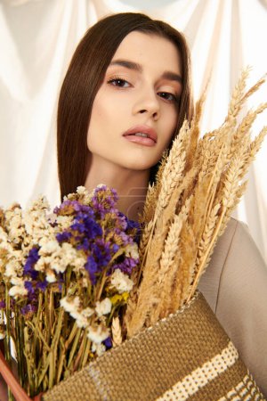 A young woman with long brunette hair, exudes a summer vibe as she holds a bouquet of dried flowers in a studio setting.