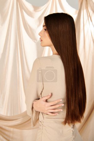 A young woman with long brunette hair stands confidently in front of a curtain, embodying a summer mood in her stylish outfit.