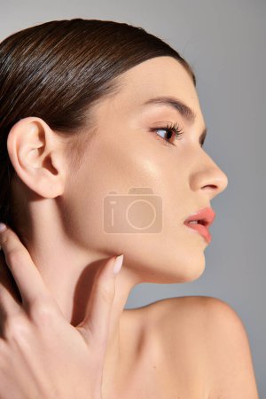 A young woman with brunette hair softly places her hand on her neck while posing in a studio setting on a grey background. magic mug #709767566
