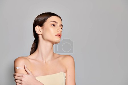 Téléchargez les photos : Une jeune femme aux cheveux bruns pose dans une robe sans bretelles, serrant doucement son épaule. - en image libre de droit