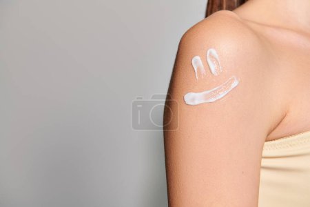 Photo for A young woman with brunette hair is showcasing a smile drawn on her arm in a studio setting against a grey background. - Royalty Free Image