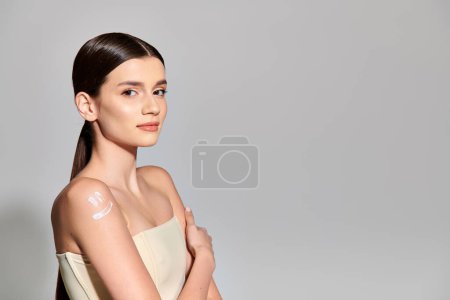 Téléchargez les photos : Une jeune femme brune pose élégamment dans une robe blanche sur fond gris dans un décor de studio. - en image libre de droit