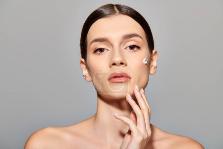 A brunette woman with clear skin delicately touches her face with face cream exuding confidence and elegance.
