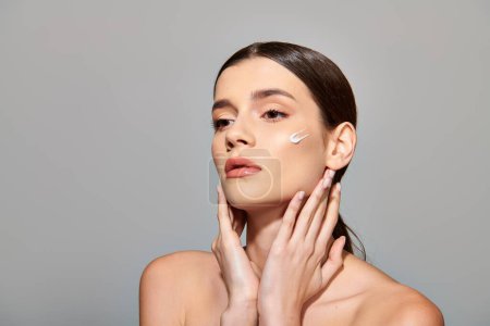 A young woman with brunette hair applies cream on her face exuding beauty and self-care.